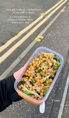 a person holding up a plastic container filled with food on the side of the road