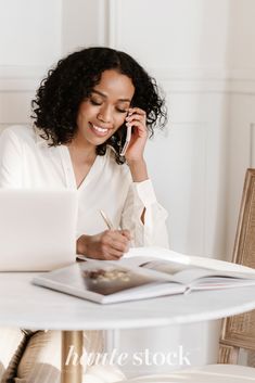 a woman sitting at a table talking on her cell phone and writing in a notebook