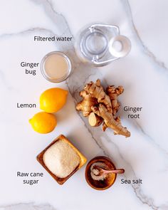 ingredients to make ginger tea laid out on a marble counter top, including lemons, ginger, ginger and sugar