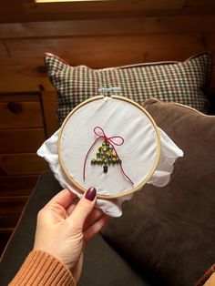 a person holding up a cross stitch christmas tree ornament in front of a pillow