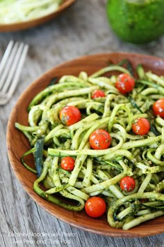 a wooden bowl filled with zucchini noodles and tomatoes on top of a table