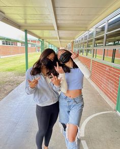 two young women walking down a sidewalk with their hands in the air while wearing masks