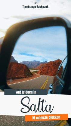 the side view mirror of a car on a road with mountains in the back ground