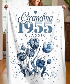 a woman is holding up a white banner with blue flowers and the words grandma 1953 classic