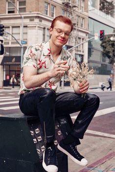 a man sitting on top of a metal box holding a bunch of dead flowers in his hands