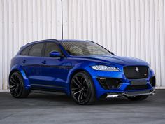 a blue suv parked in front of a white wall with black rims on it