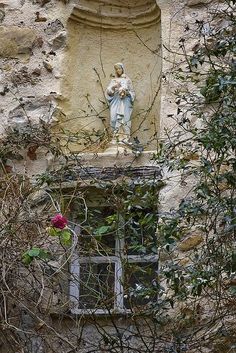 an old building with a statue on the window sill and vines growing around it