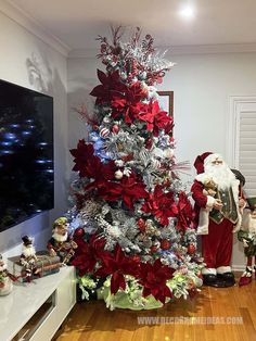 a christmas tree is decorated with red and silver poinsettis, while santa claus stands next to it