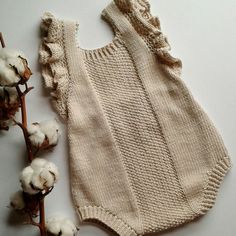 a white knitted bodysuit next to cotton flowers on a white surface with one flower in the foreground