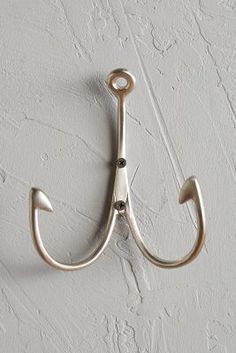 a metal hook on the side of a white wall with an umbrella shaped hook hanging from it's center