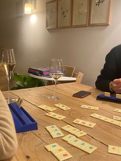 a man and woman sitting at a table with wine glasses in front of them, playing scrabble