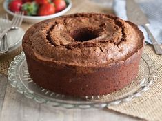 a chocolate cake sitting on top of a glass platter next to a bowl of strawberries