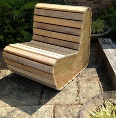 a wooden bench sitting on top of a stone floor next to plants and bushes in front of a brick wall