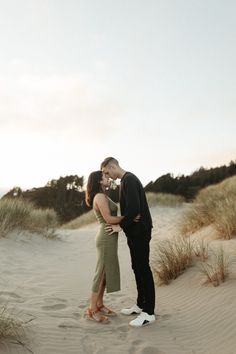 a man and woman standing in the sand with their arms around each other as they kiss