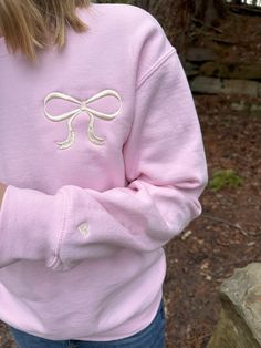 Get cozy and stylish with our Big Bow Sweatshirt! This adorable, girly sweatshirt features a cute bow design, perfect for adding a touch of style to any outfit. The sleeve has a tiny heart design on the sleeve for an extra custom touch.  Whether you're out for a stroll or lounging at home, this sweatshirt is sure to keep you looking chic and feeling comfortable. Perfect for gifting to the fashionista in your life! A soft 50/50 sweatshirt (cotton and polyester) is machine embroidered with the des Casual Long Sleeve Bow Sweater, Casual Long Sleeve Sweater With Bow, Cute Long Sleeve Fleece Tops, Trendy Pink Fleece Sweater, Cute Pink Long Sleeve Sweatshirt, Cute Long Sleeve Pink Sweatshirt, Sweet Long Sleeve Cotton Sweatshirt, Pink Sweatshirt For Loungewear, Spring Preppy Cotton Sweater