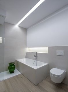 a white bathroom with a green vase on the counter next to the bathtub and toilet