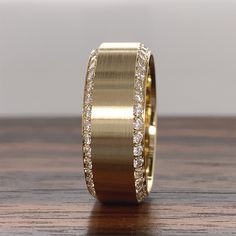 a gold wedding band with white diamonds on the inside and outside, sitting on a wooden surface