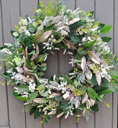 a wreath with white flowers and greenery hanging on a wooden wall next to a door