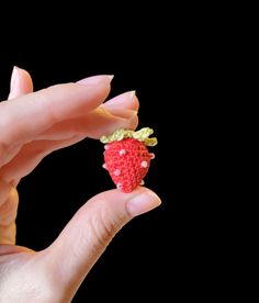 a hand holding a tiny toy strawberry in it's left hand, against a black background