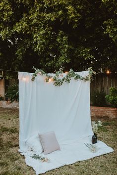 a white sheet draped over a bed with greenery on it in the backyard at night