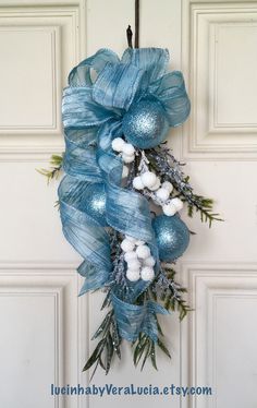 a blue christmas wreath hanging on the front door with cotton balls and greenery attached to it