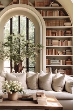 a living room filled with lots of white furniture and bookshelves next to a window