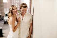 a man and woman standing next to each other in front of a white wall smiling