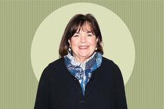 a woman wearing a black coat and blue scarf standing in front of a green background