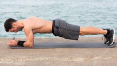 a shirtless man doing push ups on a yoga mat by the water's edge