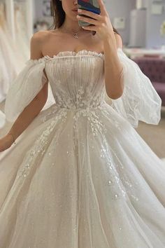 a woman taking a selfie wearing a wedding dress with sleeves and flowers on it