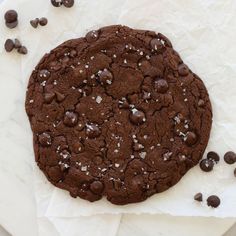 a chocolate cookie with sea salt and chocolate chips around it on top of parchment paper