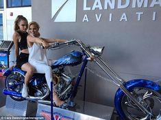 two beautiful young women sitting on a motorcycle in front of a sign that says landma aviati