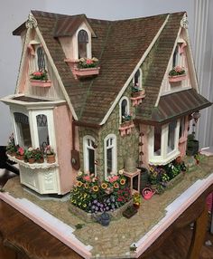 a doll house with flowers and potted plants on the front porch, sitting on top of a table