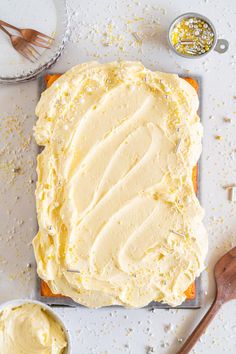 a cake with frosting sitting on top of a table next to two bowls and spoons