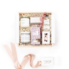 an open gift box with candles, soaps and other items in it next to a pink ribbon