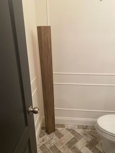 a white toilet sitting in a bathroom next to a tall wooden pole on the floor