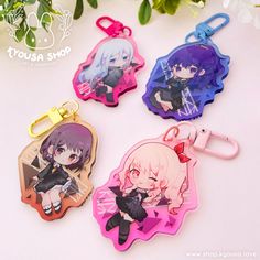 four keychains with anime characters on them sitting next to each other and flowers in the background