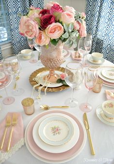 the table is set with pink and white plates, silverware, and flowers in a vase