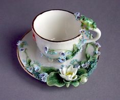 a tea cup and saucer decorated with flowers on a purple background, sitting on a plate