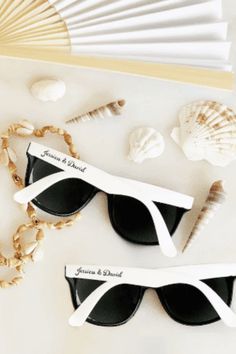 two pairs of sunglasses with personalized tags attached to them next to seashells