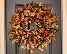 a wreath with red berries and green leaves hanging on a front door, next to a black door