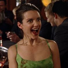 a woman in a green dress is laughing and holding a wine glass with her mouth open