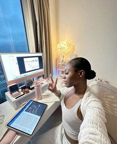 a woman sitting in front of a computer on top of a desk with a tablet