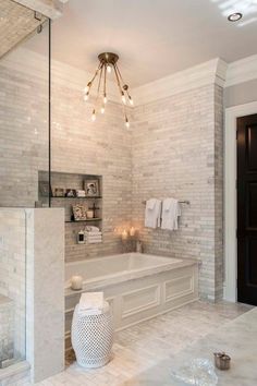 a bathroom with white marble walls and flooring, chandelier above the bathtub