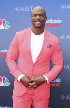 a man in a pink suit and white shirt smiles for the camera while standing on a red carpet