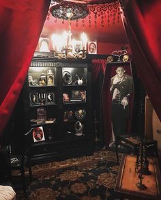 a room with red drapes and an old fashioned display case in the corner,