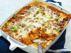 a casserole dish with meat, cheese and green onions in it on a blue towel