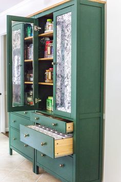 a green cabinet with drawers and shelves in the middle is open to reveal an assortment of spices