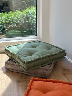 two dog beds sitting on the floor in front of a window with an orange pillow