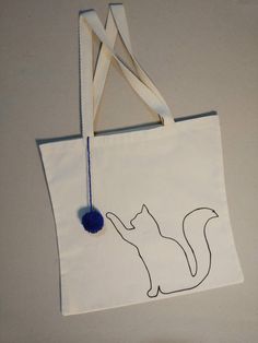 a white tote bag with a black cat on it and a blue pom - pom